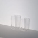 Two tall clear glass tumblers on a white surface against a white wall
