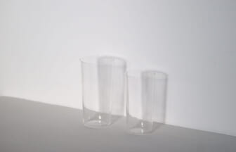 Two tall clear glass tumblers on a white surface against a white wall