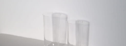 Two tall clear glass tumblers on a white surface against a white wall