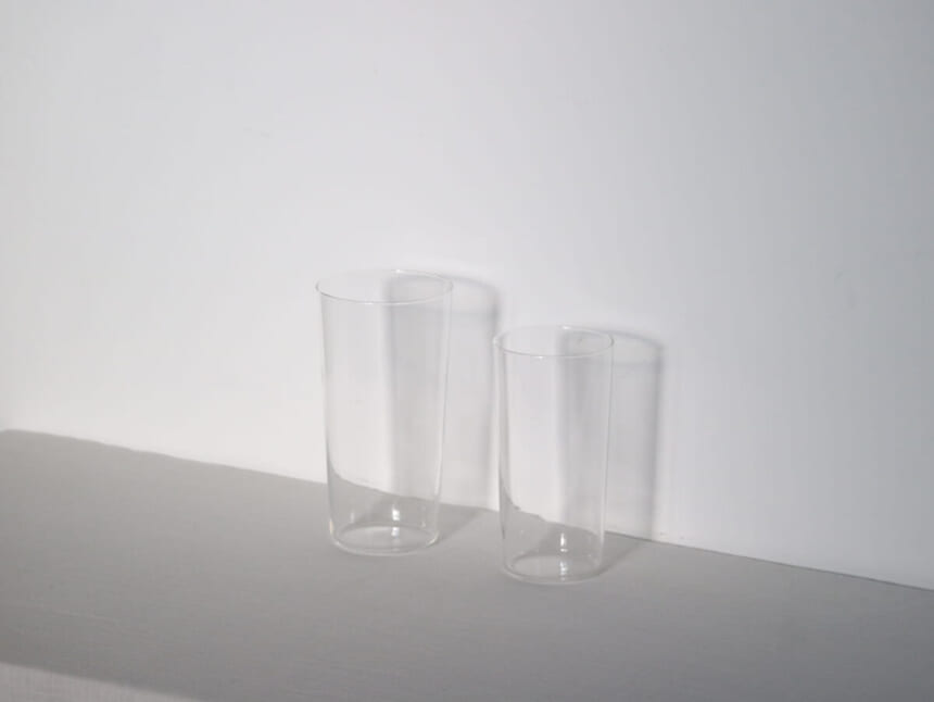Two tall clear glass tumblers on a white surface against a white wall