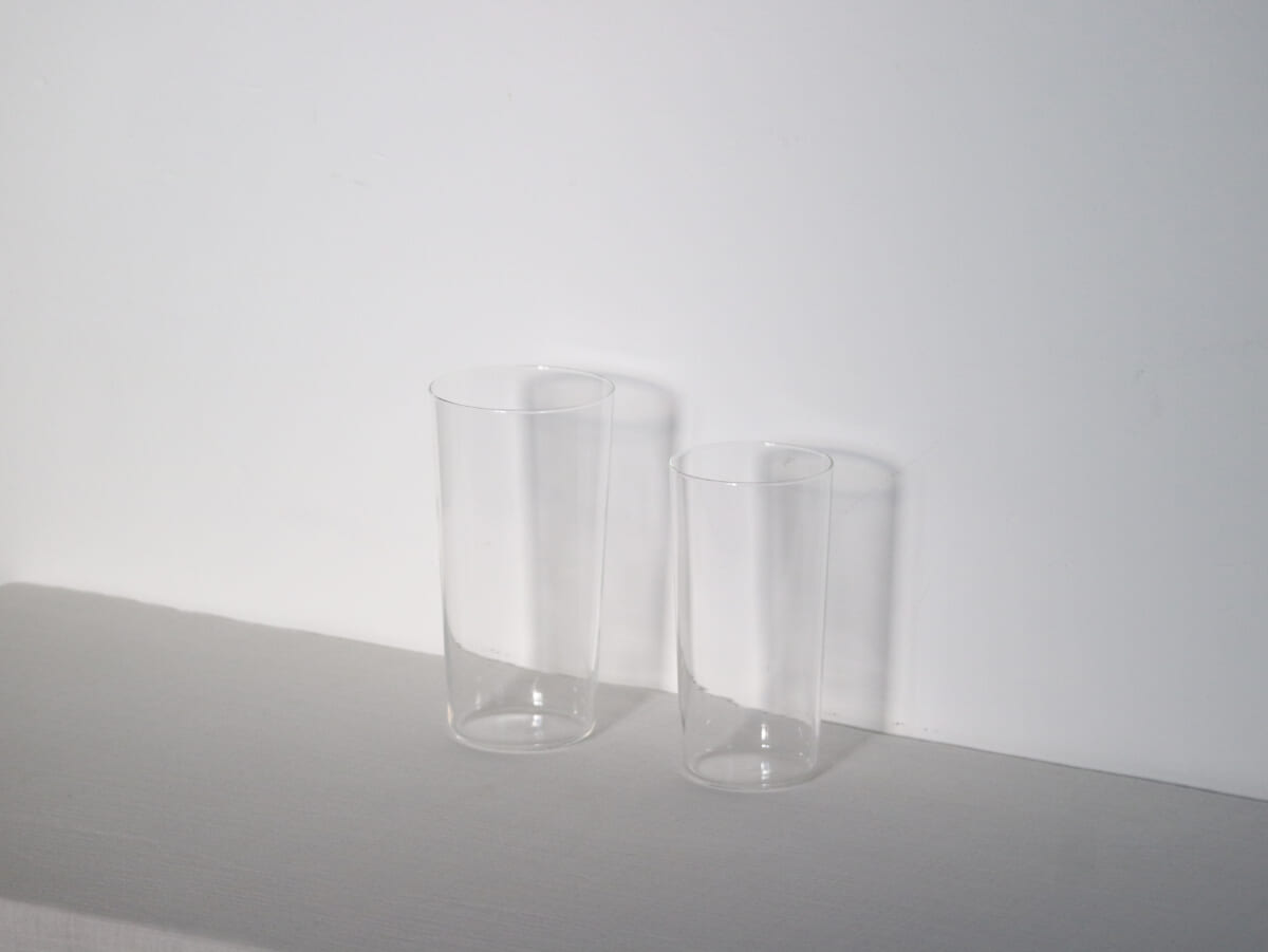Two tall clear glass tumblers on a white surface against a white wall