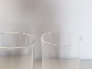 Two clear drinking glasses placed side by side on a light surface with a soft gray background