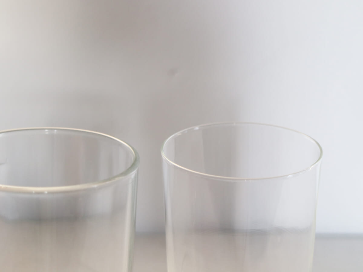 Two clear drinking glasses placed side by side on a light surface with a soft gray background