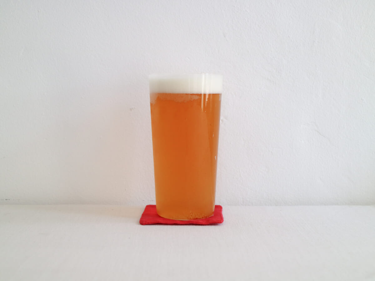 Tall pint of amber beer with a white foamy head on a red coaster against a white wall