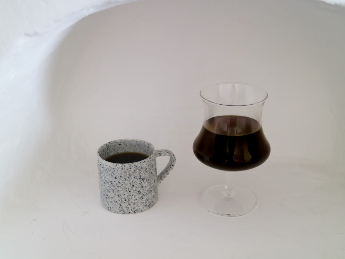 IMG4399 | コーヒーステーション Speckled gray ceramic mug filled with black coffee beside a stemmed glass of dark coffee on a white surface