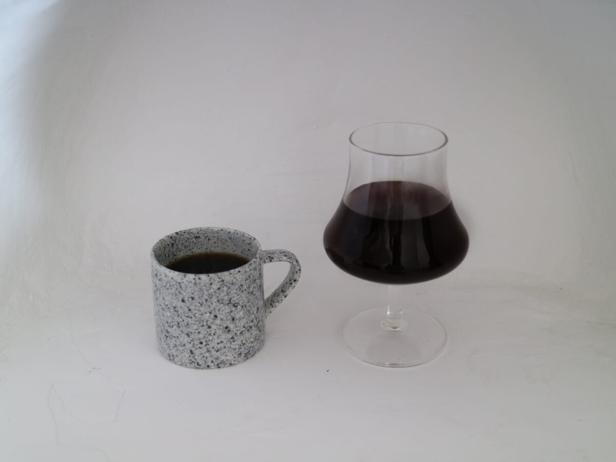 IMG4401 | コーヒーステーション Speckled ceramic mug with coffee beside a tulip shaped glass of red wine on a white surface