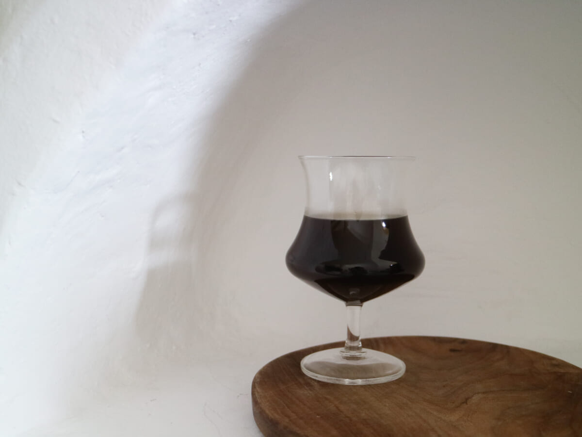 IMG4407 | コーヒーステーション A snifter glass with dark stout on a wooden round table against a plain white wall