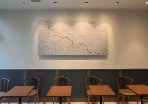 Interior of a cafe with wooden chairs and square tables a large abstract painting of a meandering black line on a pale background above dark wainscoting