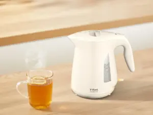 White electric kettle on a wooden table beside a steaming glass mug of tea