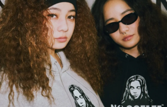 Two women with long curly hair pose together, wearing gray and black hoodies that read 'NO COFFEE' with a graphic portrait.