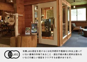 Cozy wooden cafe interior with a glass walled coffee station and a JAS certification banner at the bottom left