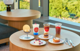 Table set with assorted desserts and drinks cream puff cake berry topped pastry ice cream sundae and three beverages in clear cups on a wooden table by a sunny window
