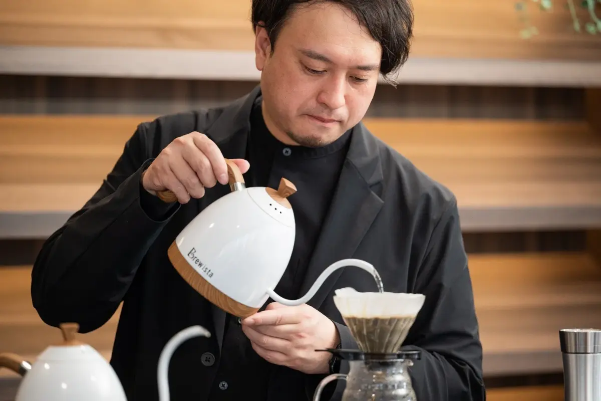 男性が白いグースネックケトルを使って、丁寧にハンドドリップコーヒーを淹れている様子。
