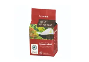 Red coffee bag with Japanese text and a pastoral image of a house in a garden on the front top features a logo and white accents suggesting a special blend