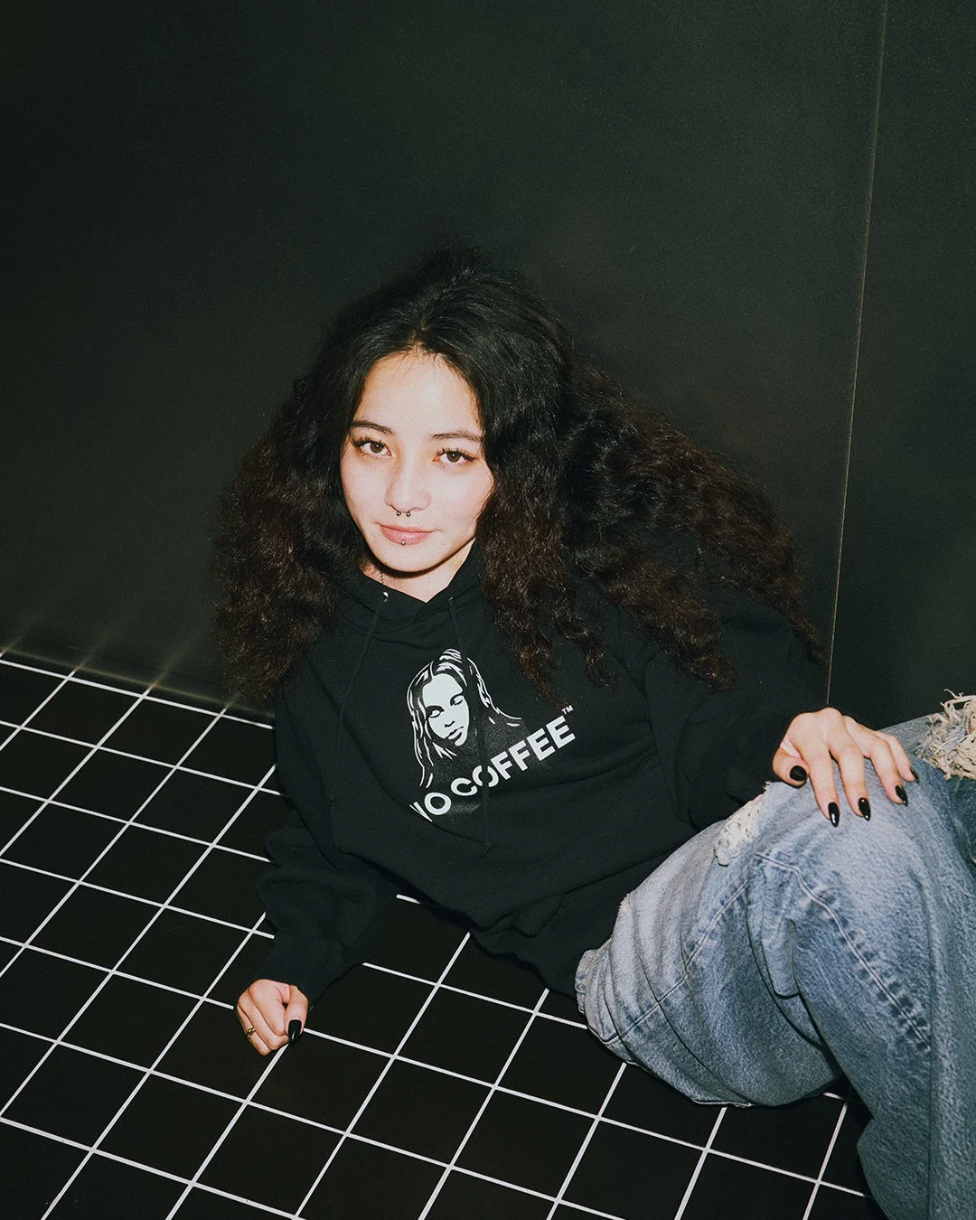 NO COFFEEのロゴ入りパーカーを着用し座る女性