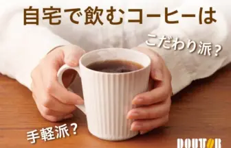 Hands hold a white mug of coffee on a wooden table with Japanese text asking if home brewed coffee should be artisanal or quick DOUTOR logo