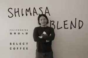 Man with arms crossed stands in front of a wall with SHIMASA BLEND and SELECT COFFEE text behind him