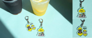 Sunlit blue table with two drinks cola and lemonade and three Becks cartoon character keychains nearby