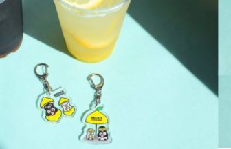 Sunlit blue table with two drinks cola and lemonade and three Becks cartoon character keychains nearby