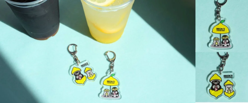 Sunlit blue table with two drinks cola and lemonade and three Becks cartoon character keychains nearby