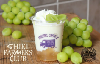 Creamy drink in a clear cup topped with whipped cream surrounded by green grapes Shiki Farmers Club branding visible on cup and background grapes nearby