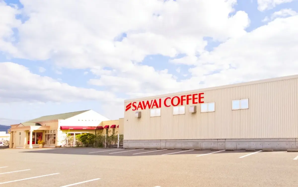 「SAWAI COFFEE」のロゴが大きく表示された建物と、その手前に広がる駐車場の風景です。