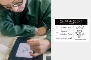 d979ee9c64e3db495eb5c3adabf17114 | コーヒーステーション A person wearing a green jacket and glasses draws on a tablet with a stylus sketching a crown wearing figure a Shimasa Blend label is shown beside