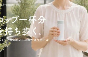 Woman in a white blouse holds a pale blue bottle on a small saucer outdoors with white Japanese promo text overlaid