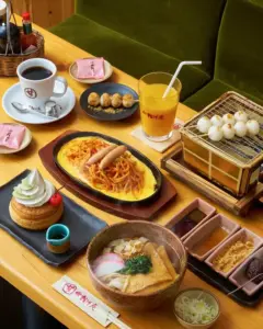 Table full of Japanese dishes omelette rice with noodles udon soup dessert pastries and dango skewers with coffee and orange juice on the side