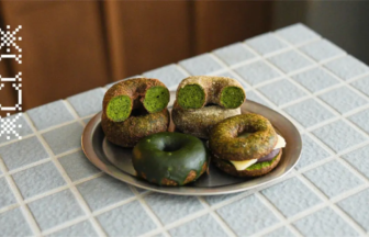 Plate of assorted matcha-green donuts on a metal dish atop a gray tiled counter; some donuts show a green interior.