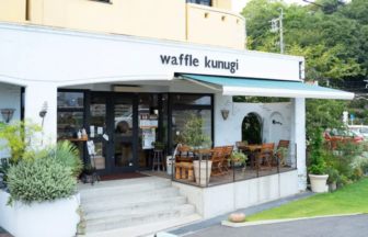 Café storefront with the sign 'waffle kunugi' and outdoor wooden seating on a covered porch.