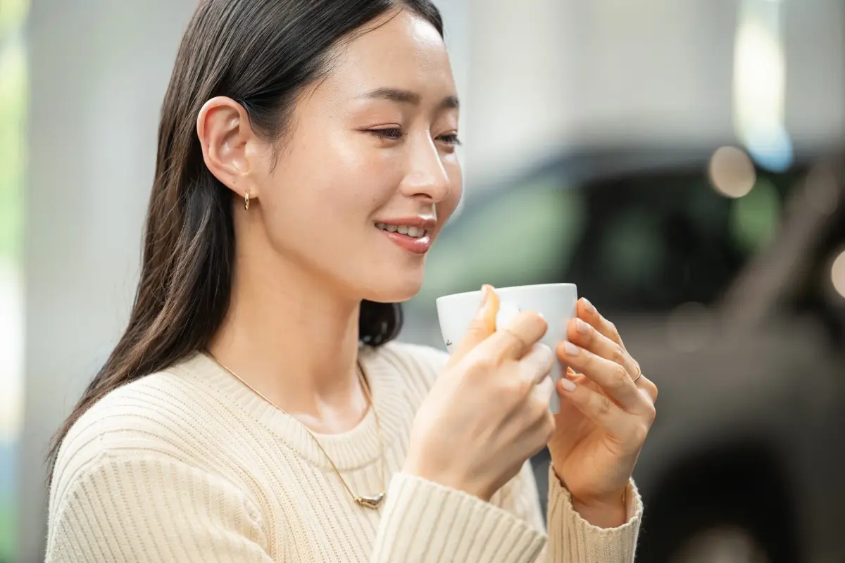 白いカップを両手で持ち、目を閉じて穏やかに微笑む女性のポートレート。