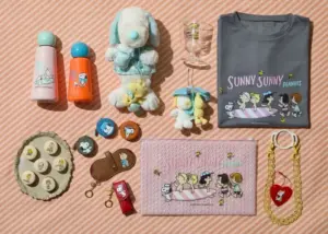 PeanutsSnoopy themed flat lay plush toys a gray Sunny Sunny Peanuts T shirt pink zip pouch assorted pins keychains and decorative accessories on a peach striped background