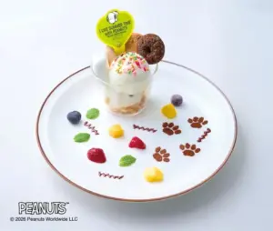Ice cream sundae in a glass cup on a white plate decorated with paw prints mint leaves berries mango cubes and chocolate swirls with a yellow heart sign on top