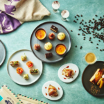 Overhead view of assorted pastries and desserts on colorful plates with coffee cups and beans on a teal table surface