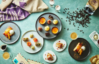 Overhead view of assorted pastries and desserts on colorful plates with coffee cups and beans on a teal table surface
