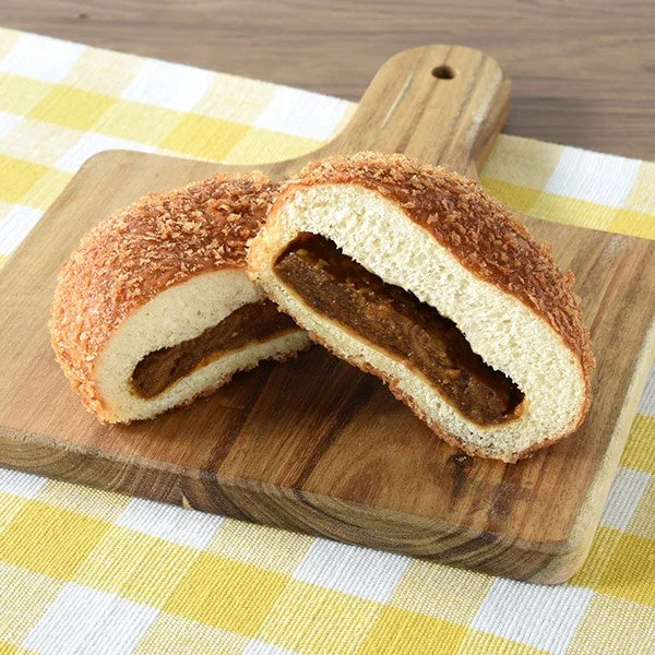 木製のカッティングボードに置かれた、半分にカットされたカレーパンの画像です。
