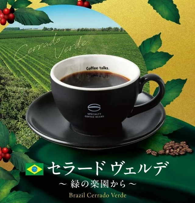 広大な緑の農園を背景に、湯気の立つ黒いコーヒーカップが置かれた画像です。カップには「Coffee talks.」と「SPECIALTY COFFEE BEANS」の文字があり、ブラジル産の「セラード ヴェルデ」というコーヒーが「緑の楽園から」と紹介されています。