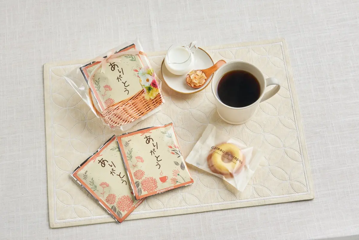 ありがとうのメッセージが書かれたドリップコーヒーと、焼き菓子、カップに入ったコーヒー、ミルク、砂糖がテーブルに並べられています
