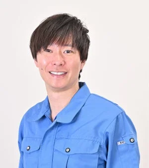 青い作業着を着た男性が、カメラに向かって笑顔を見せている